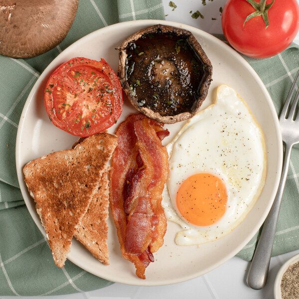 
Śniadanie w stylu brytyjskim z boczkiem, jajkiem smażonym, pieczarką portobello i pomidorem.